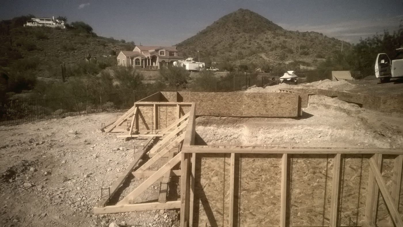 Timber footings framed up on a graded pad, a desert peak standing behind the houses.