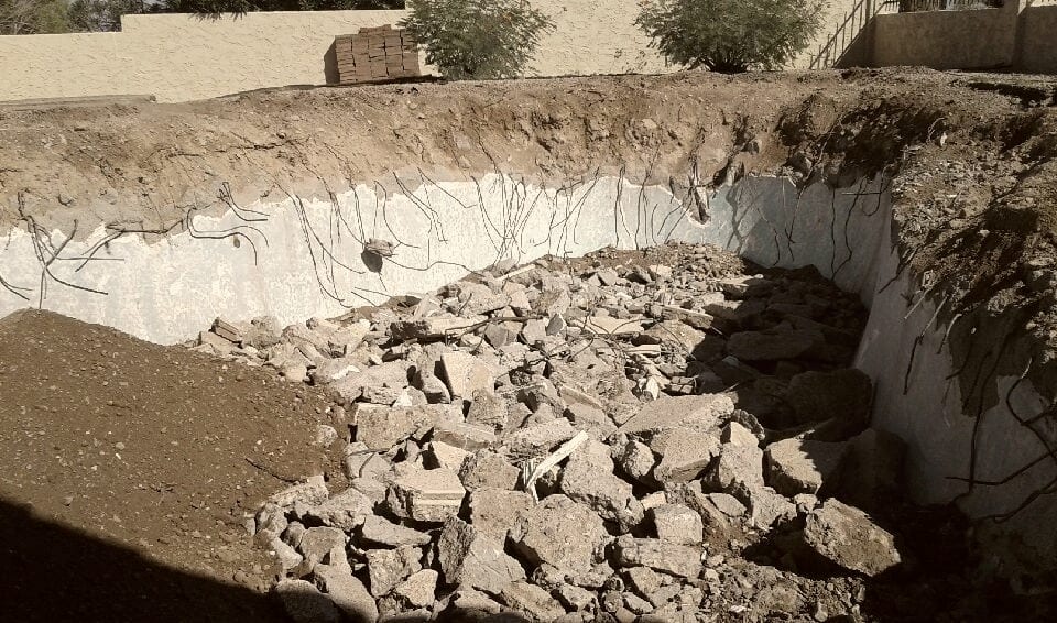 The cavity backfilled with the pool's own broken concrete, a run of the old shell still standing at the edge.